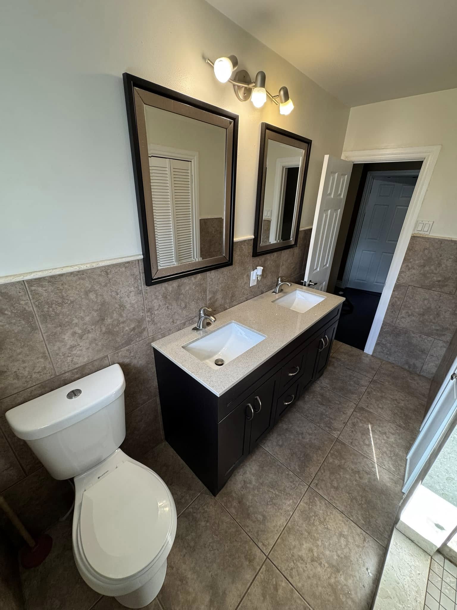 Bathroom with a dark double vanity, two mirrors and stone-look tile.