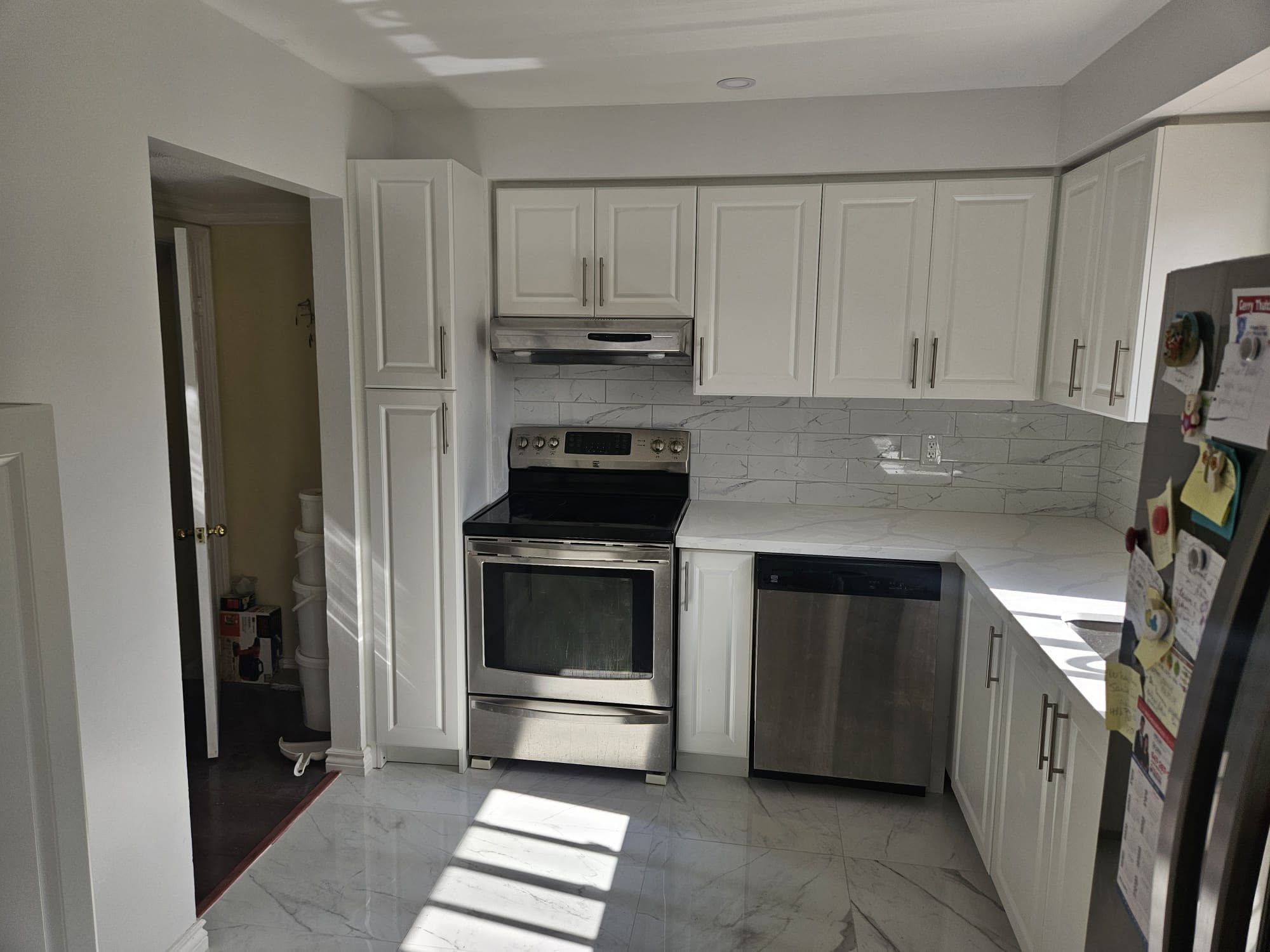 Finished kitchen with white shaker cabinets, stainless range and marble-look tile floor.